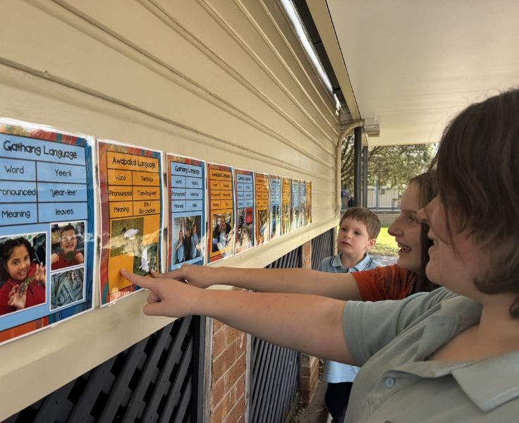 Three students pointing at a bright sign on the outside of a building