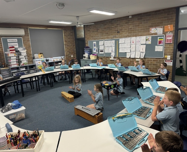 Students sitting at desks in a circle with glockenspiels in front of them